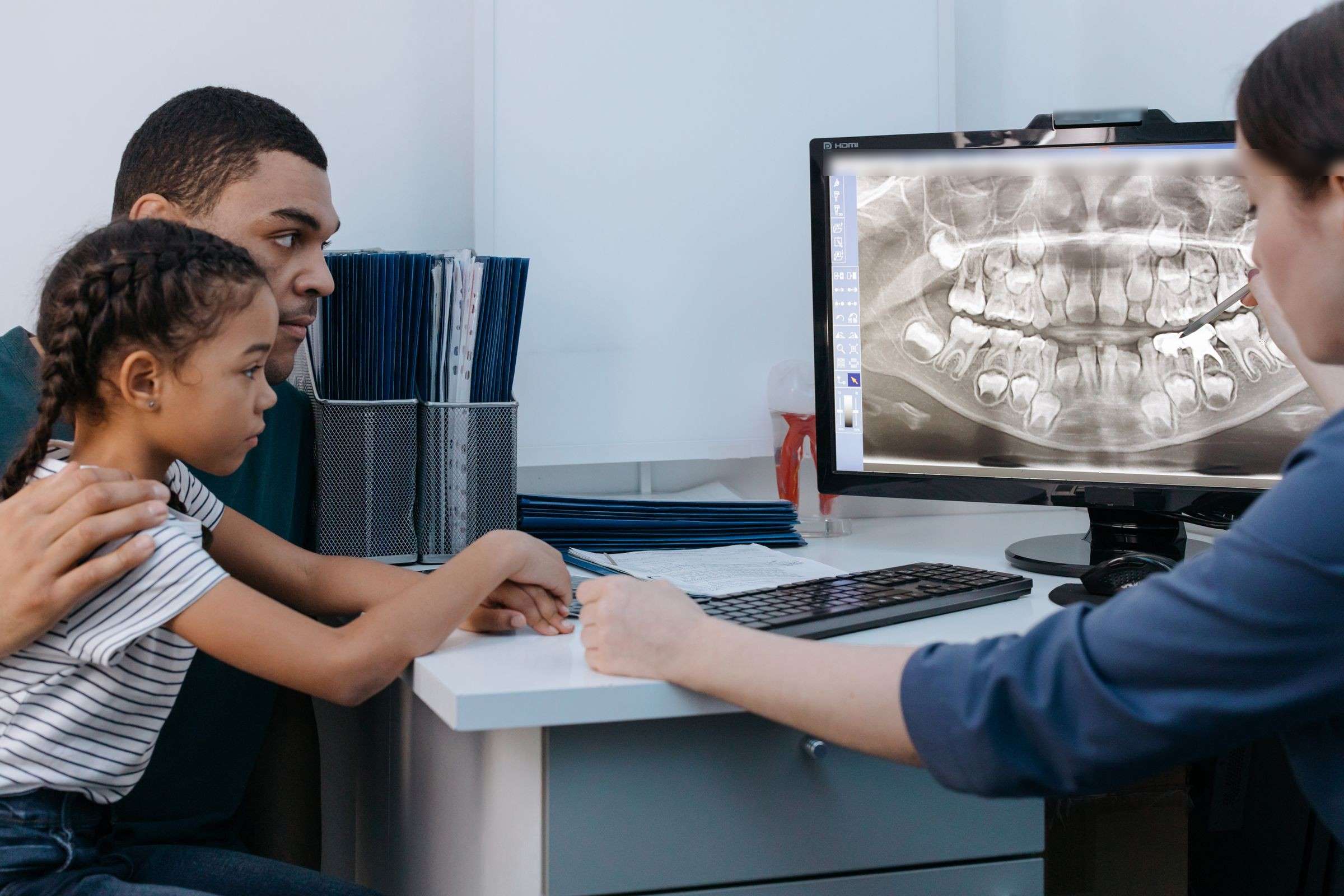 A dad and his daughter look at her X-ray on the screen while the dentist points to one tooth