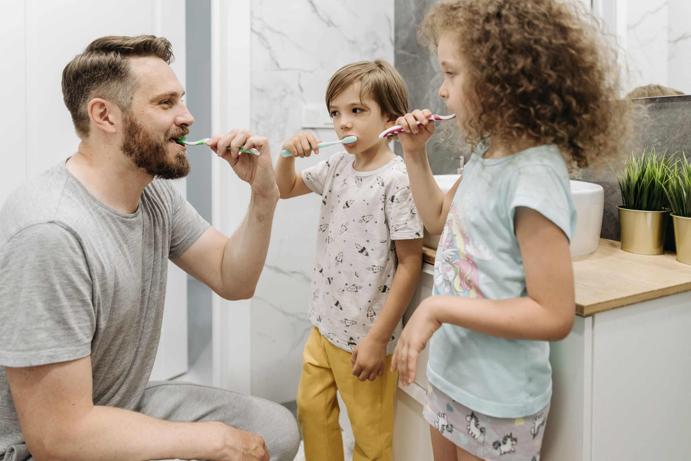 A dad and his two kids brushing their teeth together at the bathroom sink