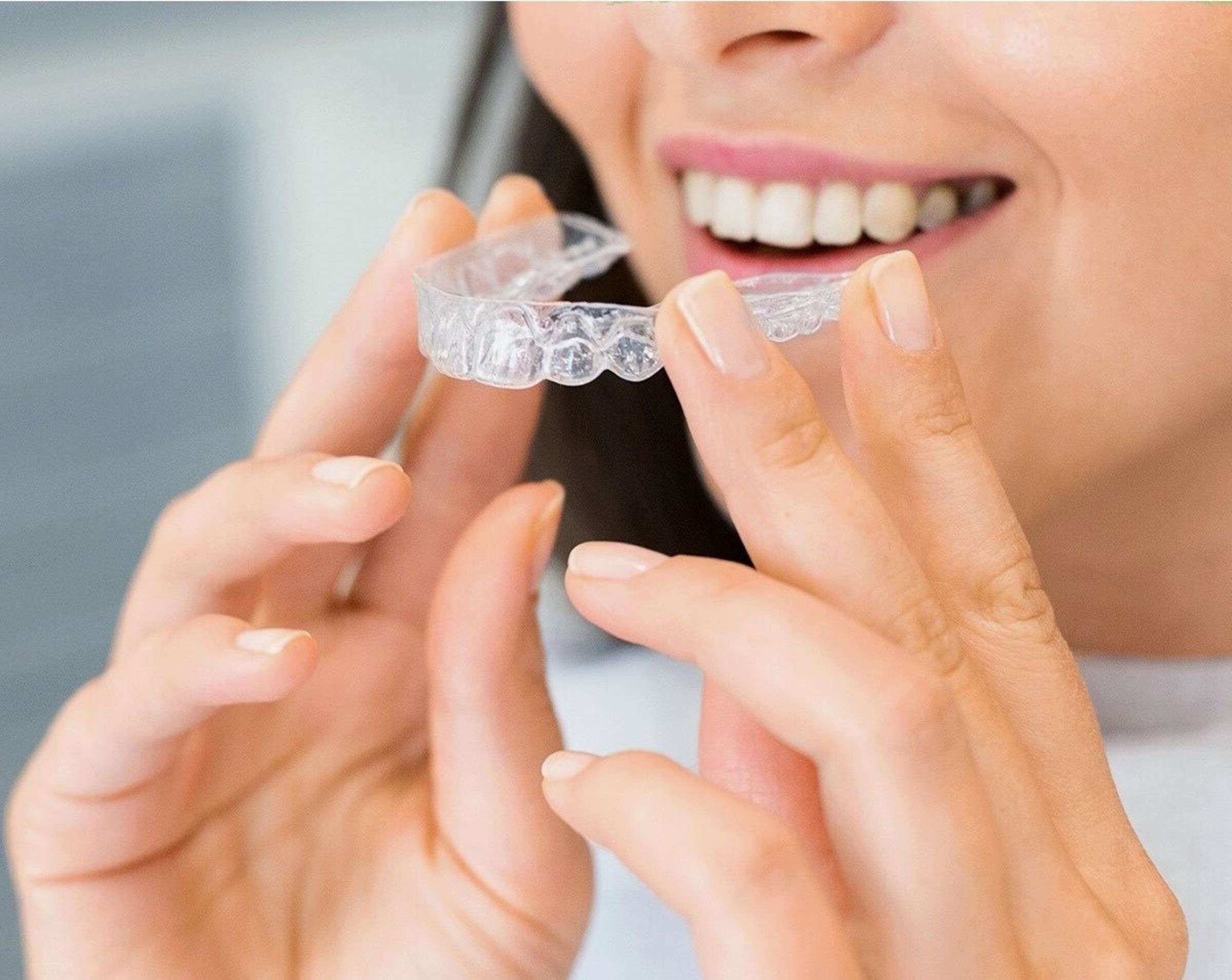 A smiling woman puts in a clear aligner