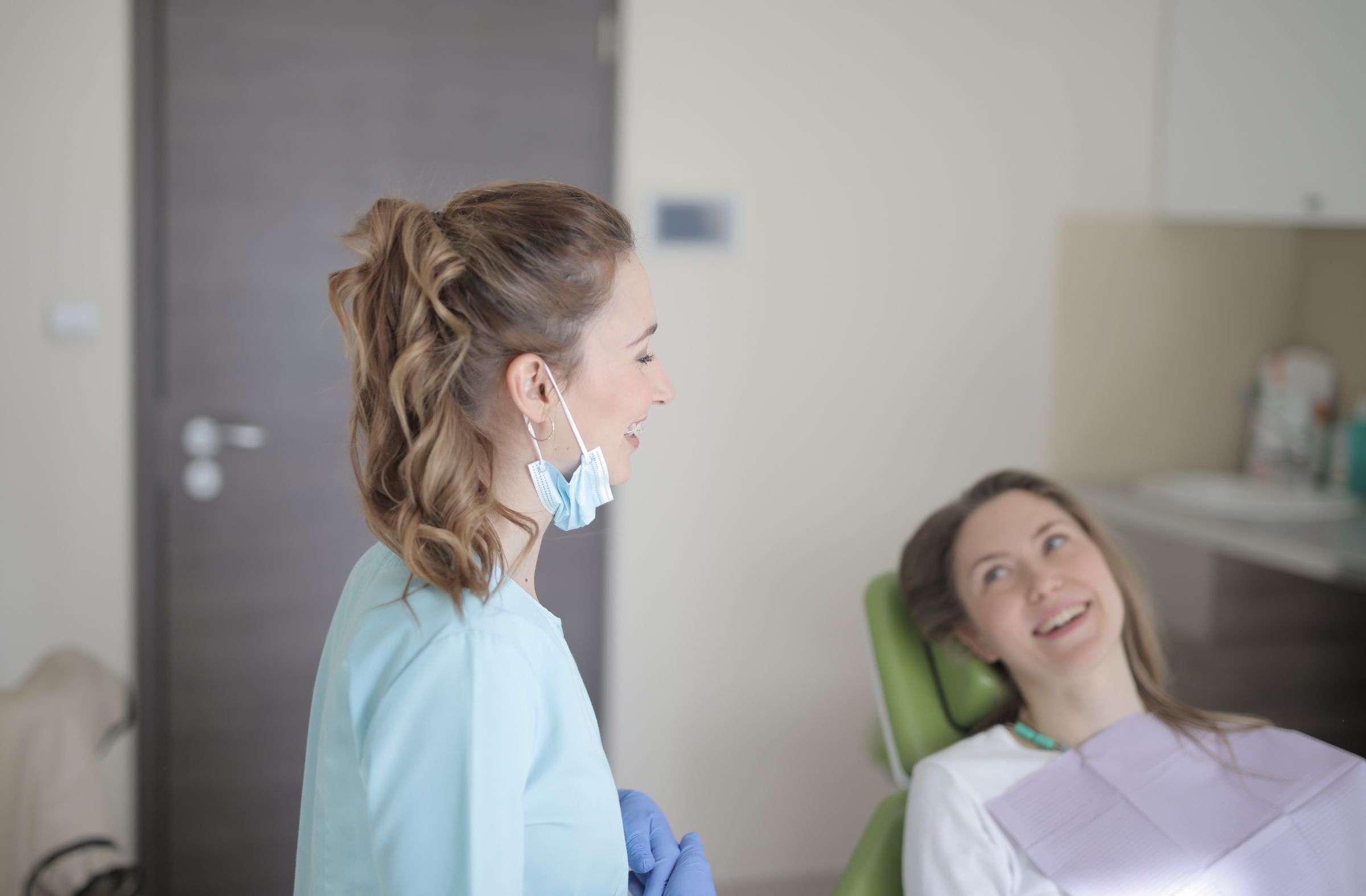 A hygienist with her mask down chats with a relaxed patient in the chair