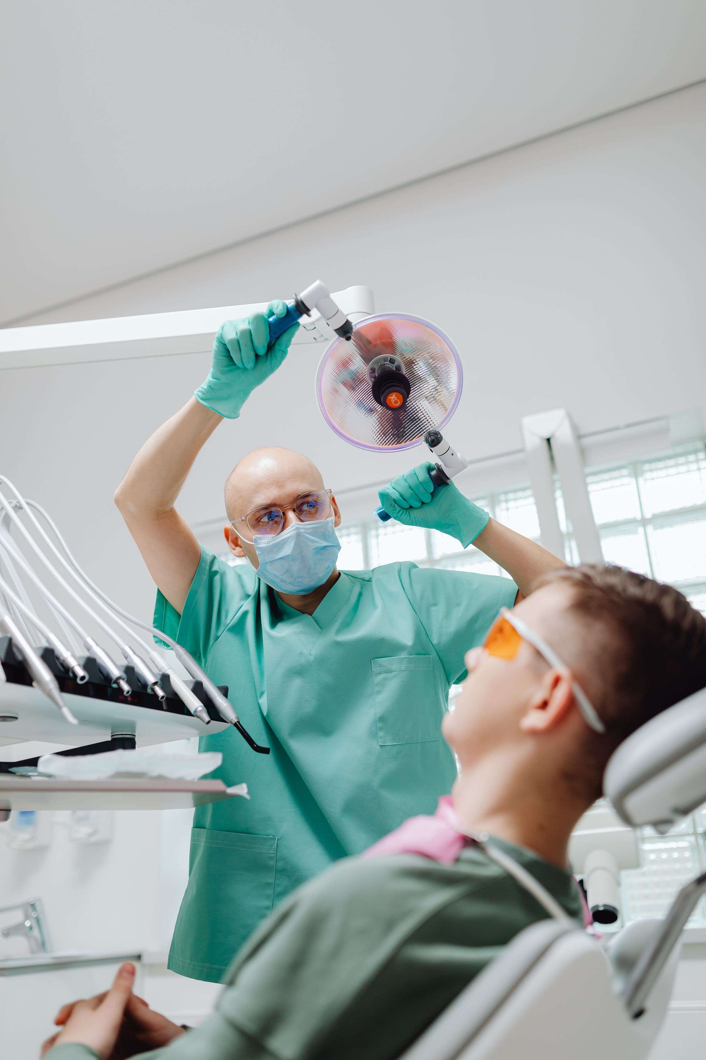 A dentist adjusts the exam light over a calm patient in a bright treatment room